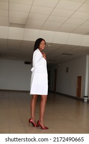 Indoor Image Of Young Black African Female Medical Professional Wearing White Coat Uniform And Holding Stethoscope Standing In Clinic Hall. Concept Of Racial Bias And Underserved Communities Society