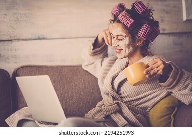 Indoor Leisure Activity At Home With Happy Woman Using Computer And Care Of Her Self With Cream On Face And Curlers On Hair. Concept Of Smart Working And Freelance People Lifestyle. Happy Female