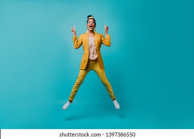 Indoor photo of lovable african girl jumping on blue background. Lovely slim lady in yellow pants funny dancing.