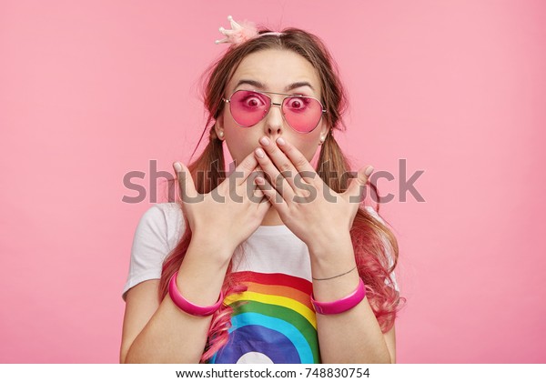 Indoor picture of shocked female lady stares with\
bugged eyes, covers mouth with hands as tries to control emotions\
and not screm loudly in surprisment, sees awful car accident on her\
own eyes