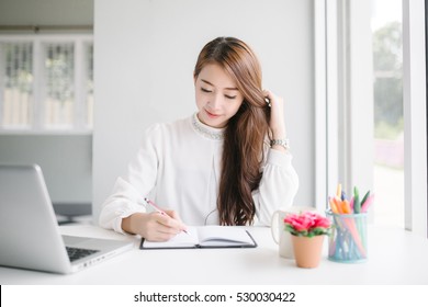 Indoor Picture Of Smiling Asia Woman Writing With Notebook And Pen