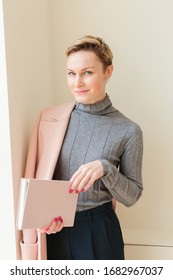 Indoor Portrait Of Beautiful Woman Wearing Pink Coat On One Shoulder, Smiling, Reading Pink Book Place Your Text For Advertising. Copy Space Mockup 