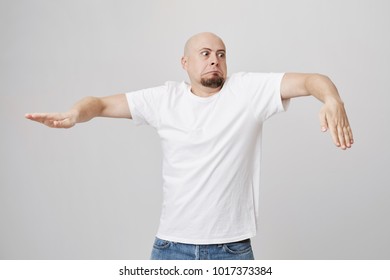 Indoor Portrait Of Funny Bald Bearded European Guy Who Is Doing Wave Dance While Standing Over Gray Background In White T-shirt And Jeans. It Is Never Too Late To Start Learning How To Breakdance