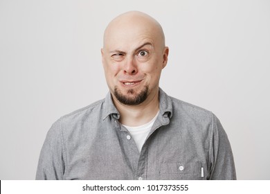 Indoor Portrait Of Funny Bald European Man Making Crazy Face While Standing Over Gray Background. Actor Performes On Stage In Play For Children. Guy Acts Weird To Avoid Conversation With Police