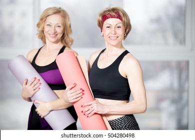 Indoor Portrait Of Group Of Two Cheerful Attractive Fit Senior Women Posing Holding Fitness Mats, Working Out In Sports Club Class, Happy Smiling, Looking At Camera With Friendly Expression