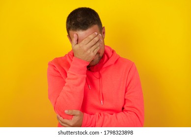 Indoor portrait of handsome man with stylish haircut, wearing casual clothes, making facepalm gesture while smiling, standing over gray background amazed with stupid situation.