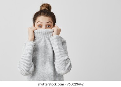 Indoor portrait of lovely woman peeking out from her jumper being amusing. Ridiculous female look from underneath of clothes girl not want to be found. Body language
