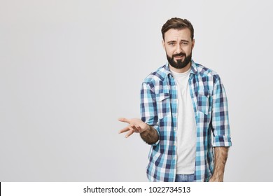 Indoor Portrait Of Mad Puzzled Guy Spreading Hand Showing Puzzled Gesture, Over Gray Background. Person Can Not Understand Why Everyone Is Bothered So Much. Maybe It Is Not A Big Deal