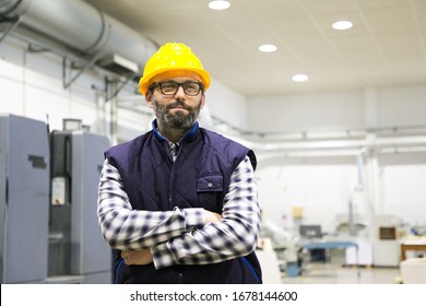 Indoor portrait of positive confident factory worker. Bearded middle aged man in glasses, hardhat and vest standing on plant floor with arms crossed and looking away. Workman concept - Powered by Shutterstock