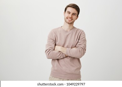 Indoor Portrait Of Positive Confident Young Businessman Standing With Crossed Hands And Adorable Smile, Being Satisfied Over Gray Background. I Achieved Everything By Myself And You Can Do It Too