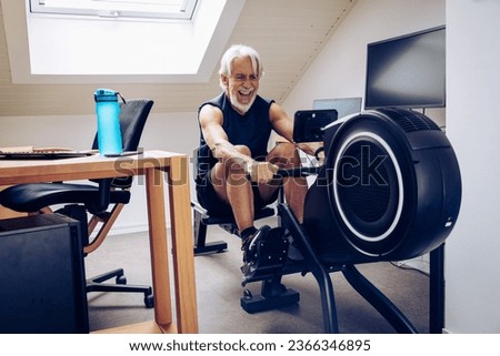 Indoor portrait of senior man working out on his rowing machine in his home office.