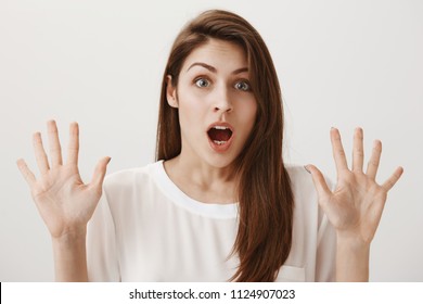 Indoor portrait of stunned and shocked attractive european woman raising palms near chest and dropping jaw from amazement as boyfriend shouts, she tries calm him down, being stuck in awkward situation