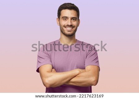 Indoor portrait of young european caucasian man isolated on purple background, standing in purple t-shirt with crossed arms, smiling and looking straight at camera