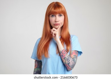 Indoor Portrait Of Young Ginger Female Posing Over White Wall Looking Into Camera With Confused Facial Expression