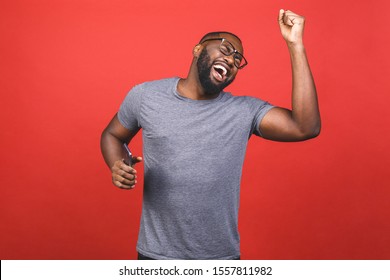 Indoor portrait of young handsome African man isolated on red background during dance to playlist he is listening from cellphone through headphones without cord, being excited.