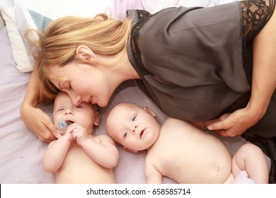 indoor portrait of young happy smiling mother with her twin babies at home