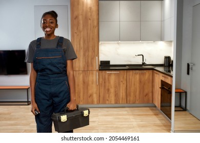 Indoor portrait of young smiling african american woman, professional technician or repairwoman posing in kitchen, holding toolkit. Female home repair service worker. Modern kitchen on background. - Shutterstock ID 2054469161