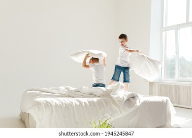 Indoor positive activity. Small children jumping on a bed and having fun fighting with pillows in sunshine - Powered by Shutterstock