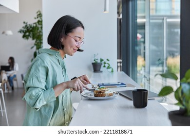 Indoor shot of Asian female model has delicious lunch in cafteria rests after online studying or freelance work uses modern technologies poses in cozy cafeteria. People and lifestyle concept - Powered by Shutterstock