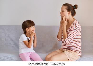 Indoor Shot Of Attractive Young Adult Speech Pathologist Working On Speech Defects Or Difficulties With Charming Girl At Home, Training For Improving Speaking, Teacher Demonstrates How To Say Sounds.