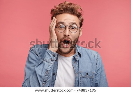 Indoor shot of bearded stylish man has trendy hairdo, looks with great surprisment, as realizes his big failure, has no right or chance for improvement. Handsome young male with shocked face