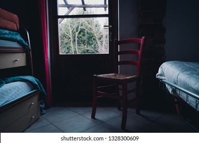 Indoor Shot Of A Bedroom With A Chair And Part Of Bed With Sunset Low Light Coming From The Window And Soft Colors