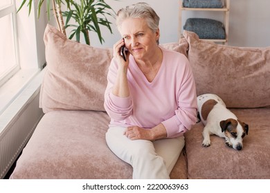 Indoor Shot Of Charming Friendly Senior Gray Haired Woman Holding Generic Smart Phone Close To Her Ear, Mature Woman Having Hearing Problem, Talking To Her Friend, Sitting Comfortably On Couch 