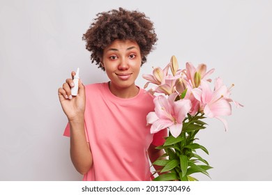 Indoor Shot Of Curly Haired Woman Holds Nasal Spray Found Proper Medicament For Stuff Nose Suffers From Allergic Rhinitis Holds Lilies Reacts On Pollen Has Red Watery Eyes. Allergy Treatment