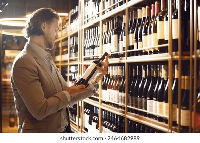 Indoor shot of experienced male sommelier taking wine bottle from shelf, choosing perfect variant for visitor based on his requests. Training for beginners wine experts.  - Powered by Shutterstock