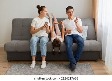 Indoor Shot Of Family Sitting On Sofa Together Father Showing Shock Content And Laughing, Woman Looking With Open Mouth And Surprised Expression, Gadget Addiction.