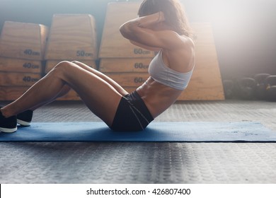Indoor shot of fitness female working out at the gym. Muscular young woman doing stomach exercises.