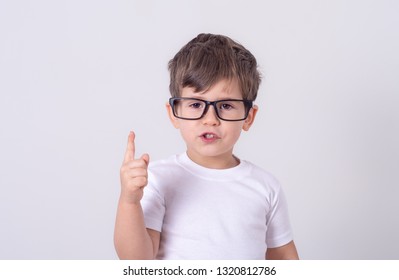 Indoor shot of friendly young boy laughing and smiling joyfully raising hands and pointing up showing copy space over grey background  - Shutterstock ID 1320812786