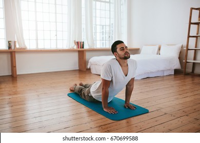 Indoor shot of handsome young man practicing yoga. Fitness man meditating with his eyes closed while doing cobra pose in living room. - Powered by Shutterstock