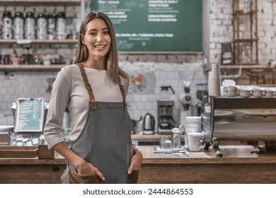 Indoor shot of happy female bar owner standing at the counter and looking in camera. Smiling young caucasian woman barista, waitress in an apron, working in coffee shop, cafe. Small business concept - Powered by Shutterstock