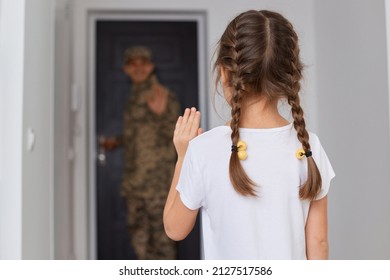 Indoor shot of military dad goes to war, little girl with dark hair and braids posing backwards and waving hand, saying good bye to father posing at the door. - Powered by Shutterstock