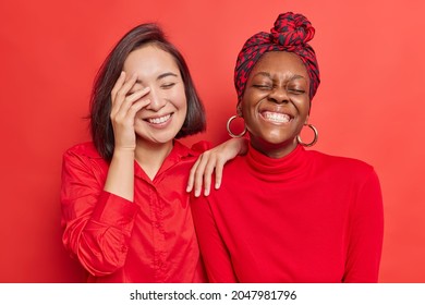 Indoor shot of overjoyed mixed race young women have fun laugh joyfully show white perfect teeth wear casual clothes isolated over vivid red background. Positive emotions and feelings concept - Shutterstock ID 2047981796