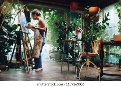Indoor shot of professional female artist painting on canvas in studio with plants. - Shutterstock ID 1139163056