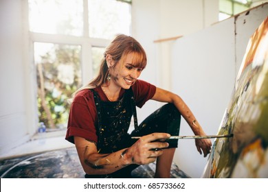 Indoor shot of professional female artist painting on canvas in studio. Woman painter painting in her workshop.