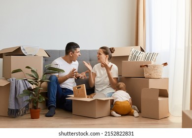Indoor shot of sad aggressive couple having argument while moving to a new house, sitting on floor near sofa and screaming, quarelling during relocation in a new apartment.