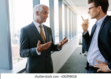 Indoor Shot Of Senior Manager Discussing Work With A Colleague. Two Businessmen Talking In Office.