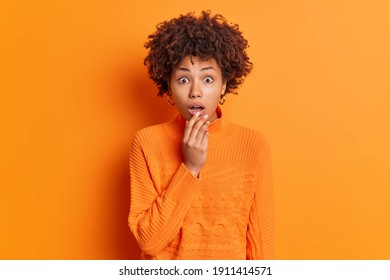 Indoor shot of shocked young curly African American woman dressed in casual jumper keeps mouth opened from amazement reacts amazing news isolated over orange background. Human reaction concept - Powered by Shutterstock