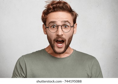 Indoor shot of surprised European man opens mouth widely, being shocked to hear horrified news, isolated over white background. Amazed excited bearded man with bated breath. Astonishment concept