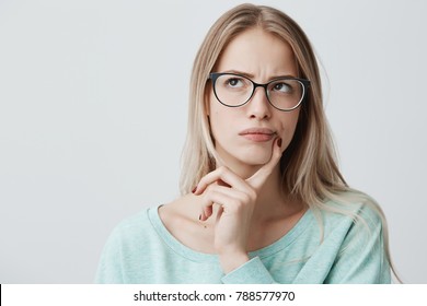 Indoor shot of thoughtful pretty woman has long blonde hair with stylish eyewear, looks aside with pensive expression, plans something on coming weekends, poses against blank wall. Puzzled female - Shutterstock ID 788577970