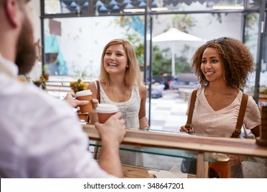 Indoor Shot Of Two Young Women Friends Smiles As They Receive Their Hot Drinks From The Cafe Counter. Happy Young Female Friends Buying Coffee.