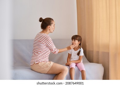 Indoor Shot Of Young Adult Female Speech Therapist Working With Little Girl, People Wearing Casual Style Clothing, Sitting On Sofa Near Window And Demonstrating How To Pronounce Sounds And Words.