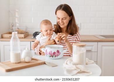 Indoor Shot Of Young Adult Girl Preparing Cake Mix In Kitchen, Mum Spending Time With Baby And Baking Together, Mommy Holding Toddler Kid In Hands, Mixing Ingredients.