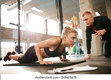 Indoor Shot Of Young Female Exercising With Personal Trainer At Gym. Fitness Woman Doing Push Ups With Her Personal Trainer At Health Club.