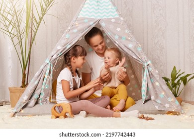 Indoor Shot Of Young Woman With Two Kids Sitting In Wigwam, Mother Playing With Preschool And Toddler Children, Clapping Hands And Smiling Happily.