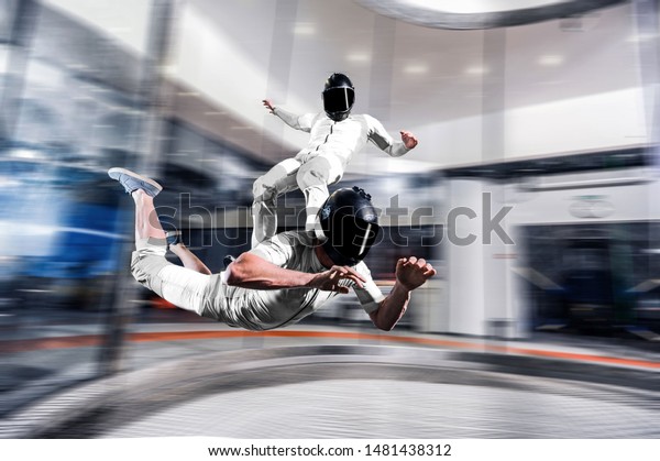 Indoor skydive tunnel. Surf sky . Men surfing on back of\
his friend. Indoor skydiving skysurfing. Free fall in wind tunnel.\
