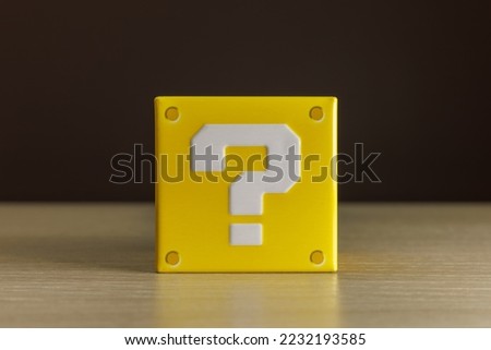 Indoor still-life photo of a little yellow box with a big white question mark printed on each face. It recalls a graphic element of a famous platform video game.